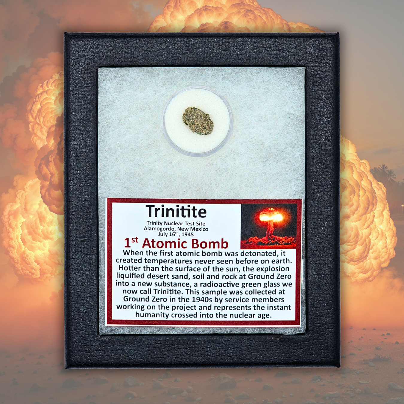 A framed historical display featuring a small circular sample of Trinitite, the first atomic bomb material, mounted on a white background with a red and black text plaque. The piece is housed in a black textured frame, set against a dramatic background of nuclear explosions.