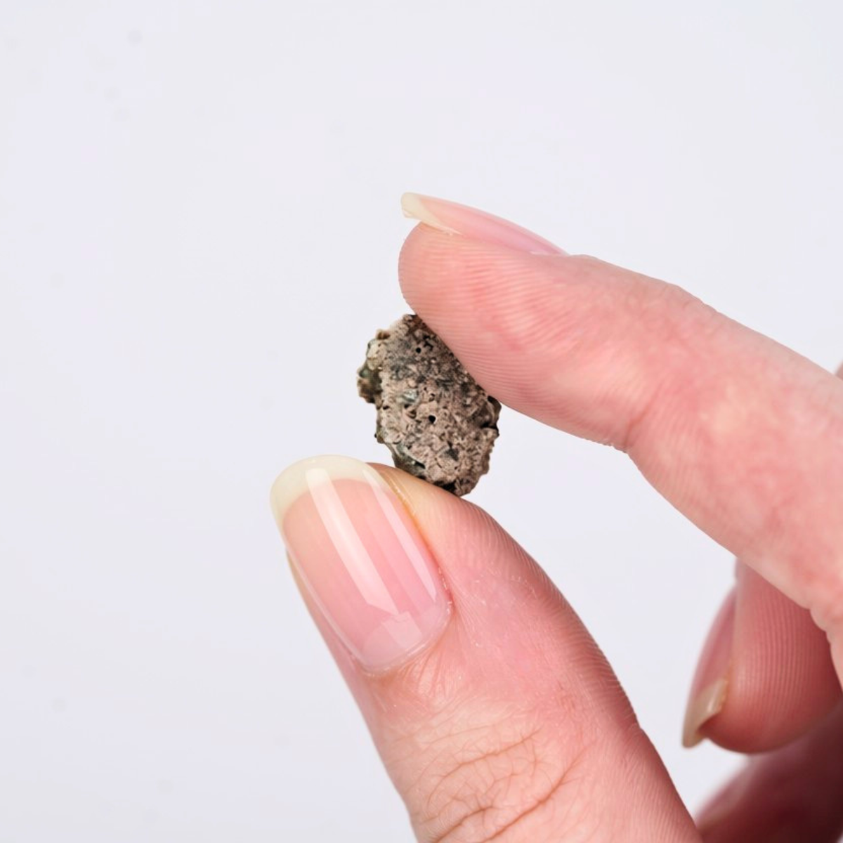 An up close image of a hand holding a piece of a trinitite specimen