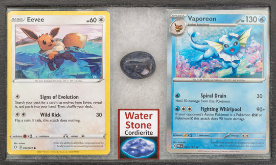 Two trading cards featuring Eevee and Vaporeon, a stone, and a card with 'Water Stone Cordierite' on a gray surface.